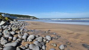 A beach with a rocky shoreline, a building with multiple floors, and a clear blue sky. - 3 Bed in Westward Ho! (oc-60678) (Westward Ho!)