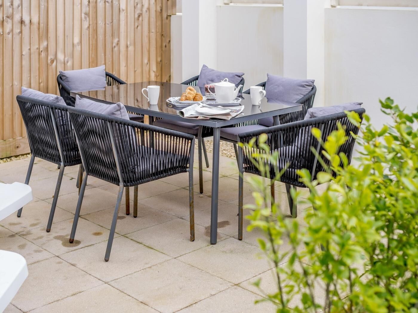 A patio with a table set for two, surrounded by four chairs.