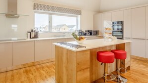 A modern kitchen with a central island, bar stools, a microwave, and a view of the neighborhood. - 3 Bed in Westward Ho! (oc-60678) (Westward Ho!)