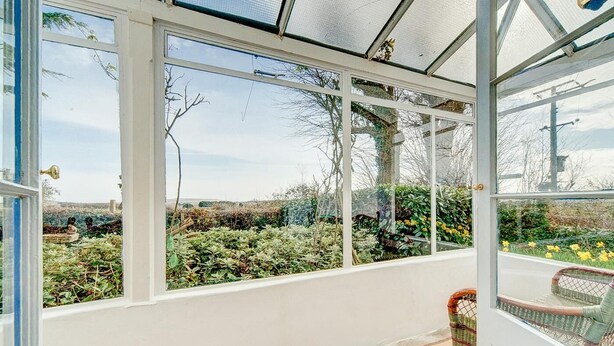 Ein Wintergarten mit großen Fenstern, einem Korbstuhl und Blick auf einen Garten.