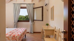 Ein Zimmer mit einem Bett, einem Schreibtisch, einem Stuhl, einem Vorhangfenster, einem Spiegel und einer Topfpflanze.
