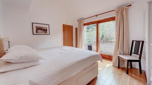 Ein Schlafzimmer mit einem Bett, einem Sessel, einem Bild an der Wand und einer Tür, die auf einen Balkon führt.