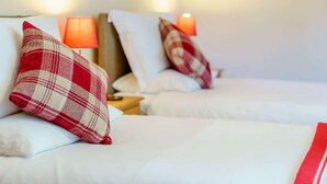 Dos camas con almohadas rojas y blancas a cuadros, una lámpara roja en cada mesita de noche y un cuadro en la pared.