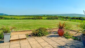 Eine Terrasse mit Steinplatten, ein großer Blumentopf und Blick auf ein grünes Feld und ferne Hügel.