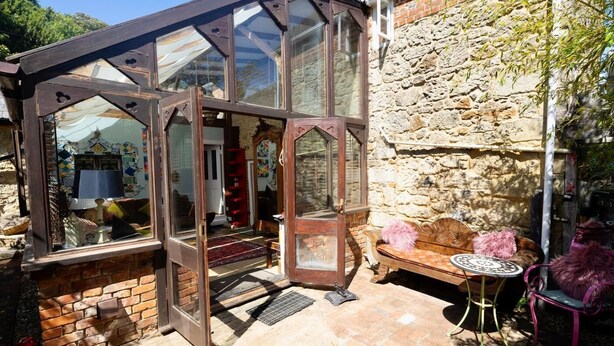 A conservatory with a glass door, a stone wall, a brick floor, and a seating area with a table and chairs. - 4 Bed in Godshill (oc-ic034) (Godshill)