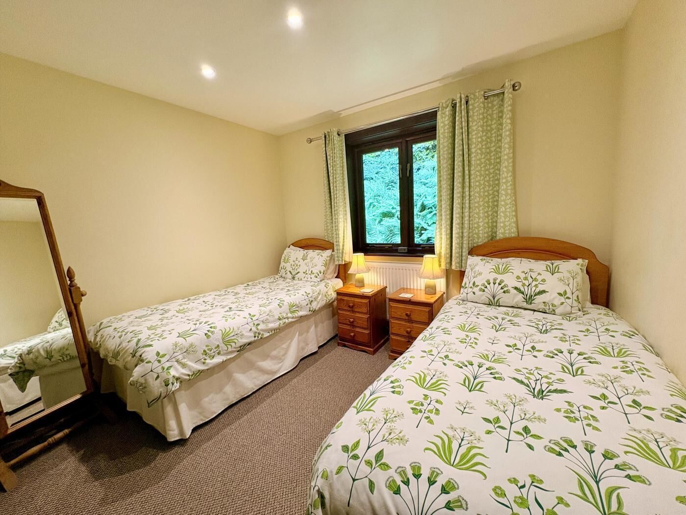 A bedroom with two single beds, a wooden wardrobe, a mirror, and a window with curtains.