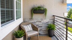 Un balcone con una sedia in vimini, una pianta in vaso, un portavaso pensile con vegetazione e un muro in pietra.