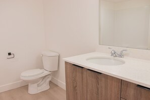 Un baño con inodoro blanco, lavamanos con espejo y armarios de madera.