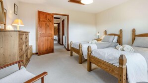 A bedroom with two wooden beds, a wooden dresser, and a hallway leading to another room. - 3 Bed in Carisbrooke (oc-ic037) (Newport)