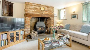 A living room with a brick fireplace, a television, a sofa, and a coffee table with magazines. - 3 Bed in Carisbrooke (oc-ic037) (Newport)