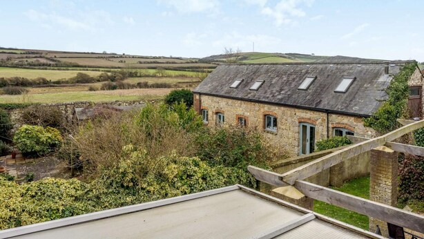 A stone building with a sloped roof, a small garden, and a view of rolling hills. - 3 Bed in Carisbrooke (oc-ic037) (Newport)