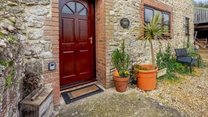 A stone building with a red door, two windows, and potted plants. - 3 Bed in Carisbrooke (oc-ic037) (Newport)