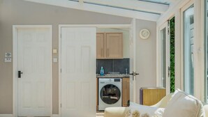 Una habitación con sofá, lavadora y zona de cocina visible a través de una puerta abierta.