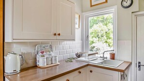 A kitchen with white cabinets, a wooden countertop, a kettle, a coffee maker, and a window with a view of trees. - 1 Bed in Cowes (oc-ic084) (Cowes)