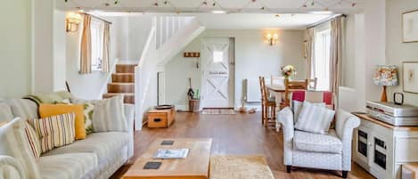 Een ruime woonkamer met een bank, fauteuil, salontafel en een trap naar een andere kamer.