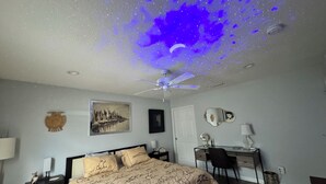 Une chambre à coucher comprenant un lit, un bureau, une chaise, un ventilateur de plafond et un miroir fixé au mur.
