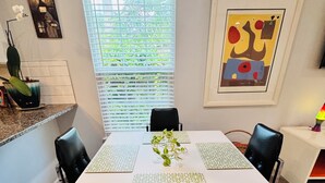 Un coin repas avec une table blanche, des chaises noires et un vase avec une plante.
