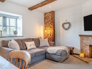 A cozy living room with a sectional sofa, a fireplace, and a wall of stacked firewood. - 2 Bed in Godshill (oc-ic085) (Godshill)