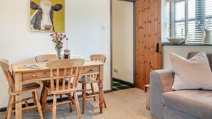 Ein gemütliches Zimmer mit einem Holztisch, Stühlen, einem grauen Sofa, einem Fenster mit Jalousien und einer Tür zu einem anderen Raum.