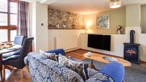 Ett vardagsrum med en soffa, ett matbord med stolar, en tv, en öppen spis och en vägg av sten.