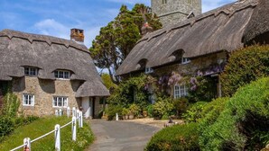 Thatched-roof cottages with stone walls, a central tower, and a paved path leading to the entrance. - 1 Bed in Godshill (oc-ic052) (Godshill)