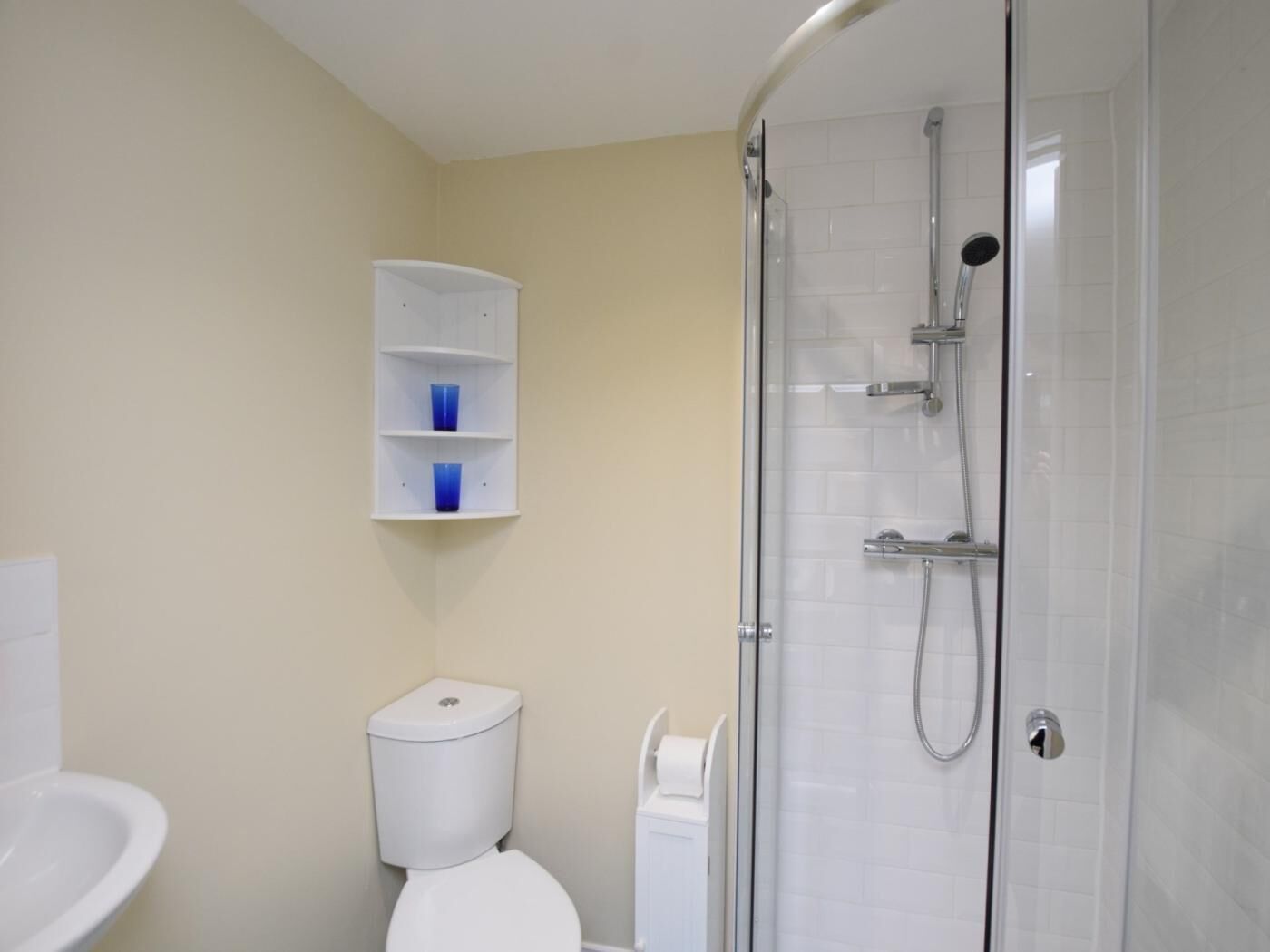 Ein Badezimmer mit Toilette, Waschbecken, Duschkabine und Ablagefläche mit zwei blauen Tassen.
