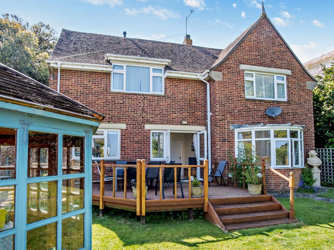 A two-story brick house with a deck, a satellite dish, and a garden.