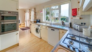 A kitchen with a gas stove, double oven, washing machine, and a view of the garden through the window. - 4 Bed in Shanklin (oc-ic068) (Shanklin)
