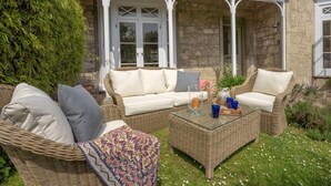 Een stenen gebouw met een overdekte patio, ingericht met rieten meubels en een glazen salontafel.