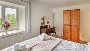 Een slaapkamer met een bed, een dressoir, een spiegel, een raam met gordijnen en een kledingkast.