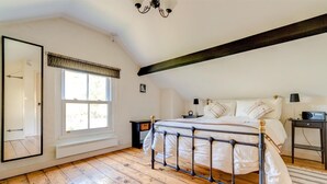 Ein Schlafzimmer mit einem Bett, einem Nachttisch, einer Lampe, einem Radio, einem Fenster mit Vorhängen, einem Spiegel und einer Heizung.