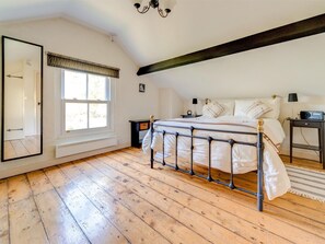 Ein Schlafzimmer mit einem Bett, einem Nachttisch, einer Lampe, einem Radio, einem Fenster mit Vorhängen, einem Spiegel und einer Heizung.