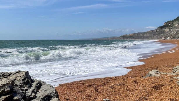 Ein Strand mit Wellen, Kieselsteinen und Klippen.