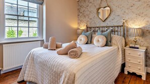 Un dormitorio con cama, mesita de noche, espejo y ventana con vistas a edificios.