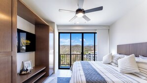 Ein Schlafzimmer mit einem großen Bett, einem Deckenventilator, einem an der Wand montierten Fernseher und einem Balkon mit Aussicht.