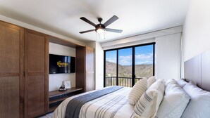 Ein Schlafzimmer mit Bett, Deckenventilator, Fernseher und einem Balkon mit Blick.