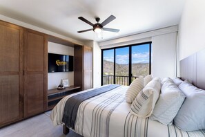 Ein Schlafzimmer mit Bett, Deckenventilator, Fernseher und einem Balkon mit Blick.