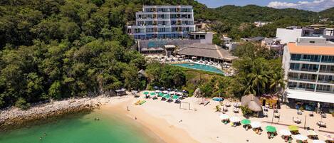 A hotel with a pool, beach, and lush greenery.
