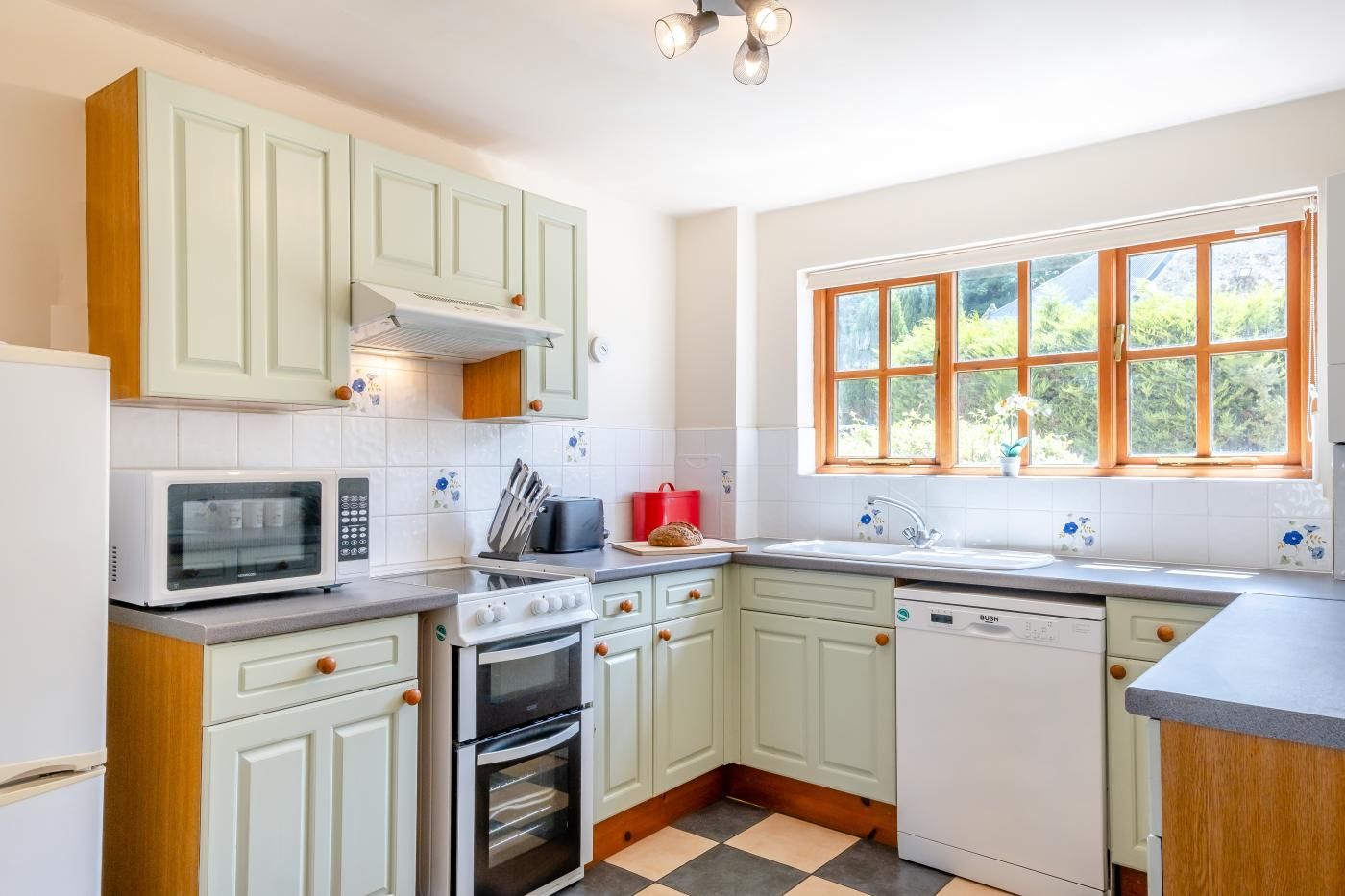 Cucina con mobili bianchi, forno a microonde, forno, lavastoviglie e finestra vista verde.
