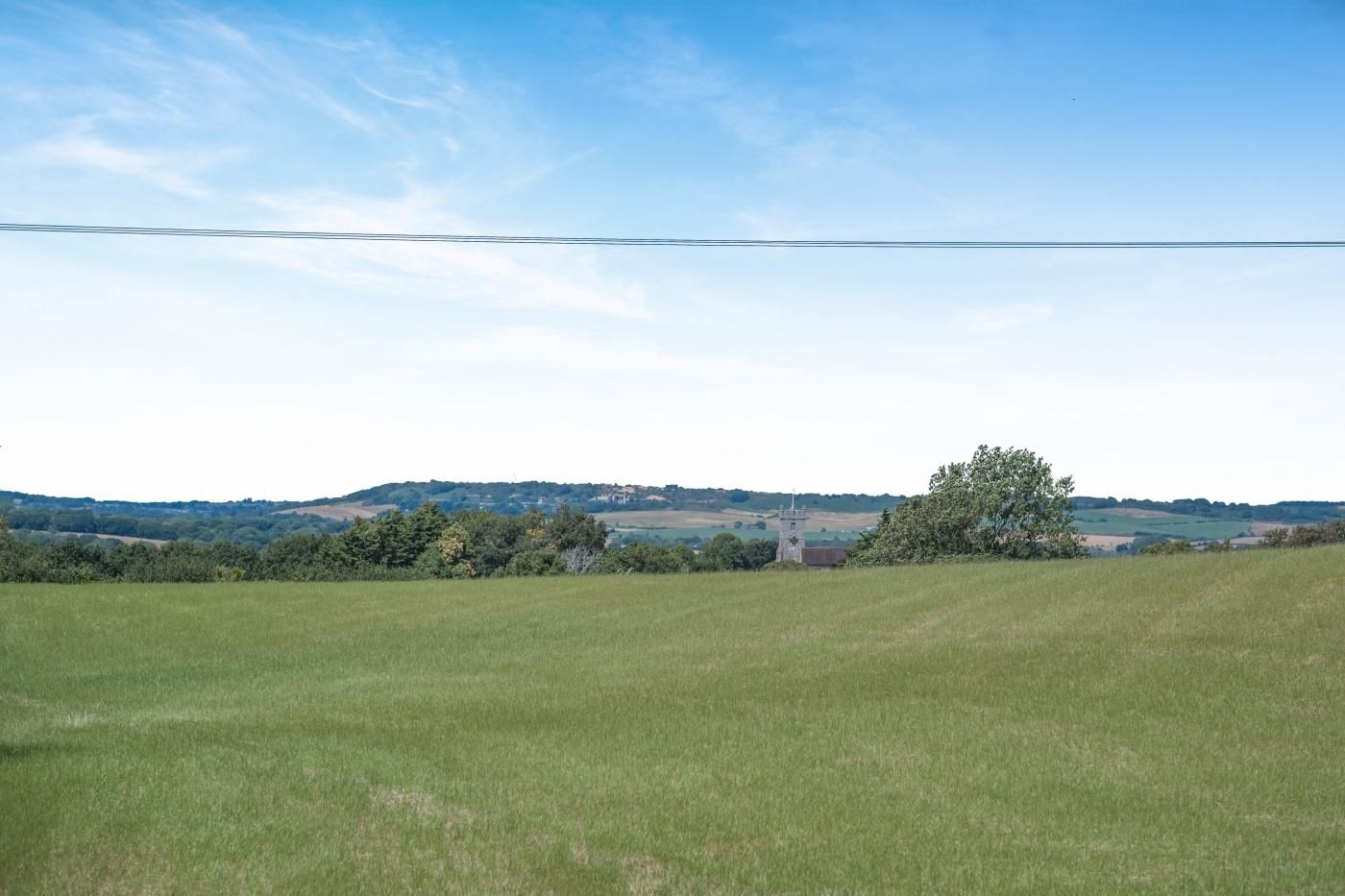 A rural landscape with a clear sky, a grassy field, and a distant building with a tower.