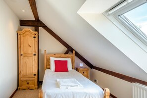 A bedroom with a sloped ceiling, a wooden wardrobe, a bed with white bedding and a red pillow, and a nightstand with a lamp. - 2 Bed in Godshill (oc-ic106) (Godshill)