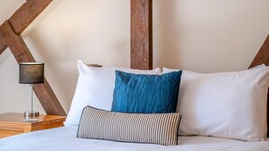 A bed with white pillows and a blue accent pillow, a striped pillow, and a bedside lamp on a wooden nightstand. - 2 Bed in Godshill (oc-ic106) (Godshill)
