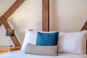 A bed with white pillows and a blue accent pillow, a striped pillow, and a bedside lamp on a wooden nightstand. - 2 Bed in Godshill (oc-ic106) (Godshill)