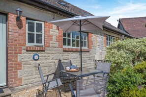 A patio with a table and chairs, a basket with bread, and a large umbrella. - 2 Bed in Godshill (oc-ic106) (Godshill)