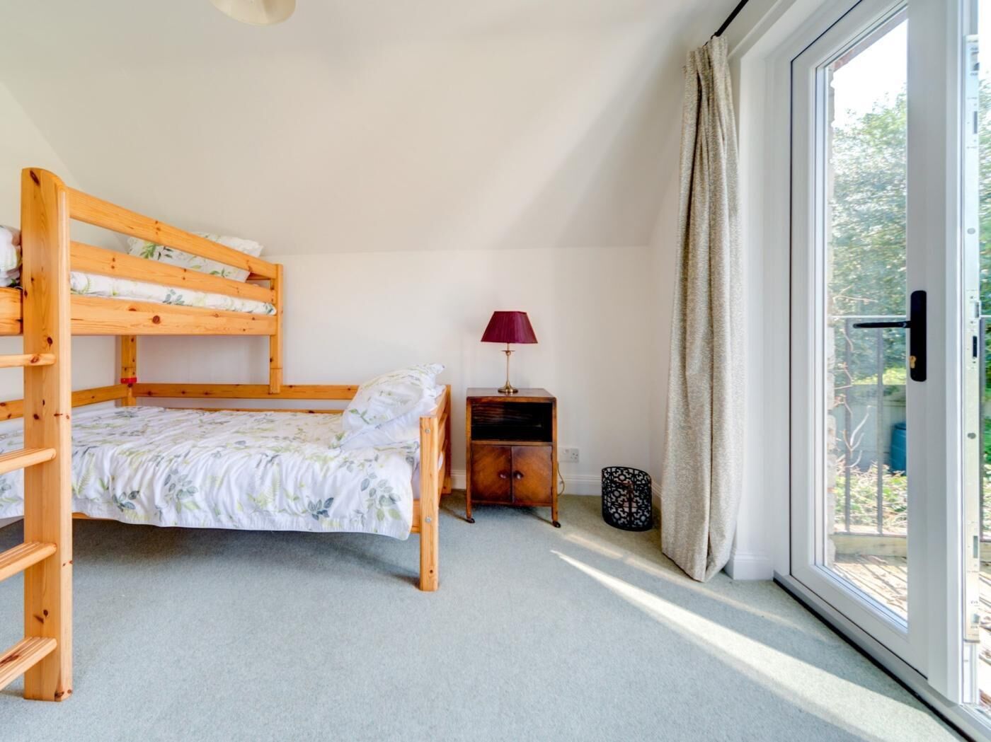 A room with a bunk bed, a bedside table with a lamp, a small cabinet, and a sliding glass door to the outside.