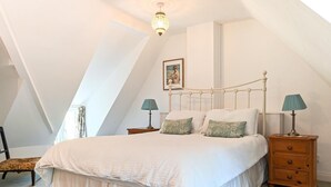 Ein Schlafzimmer mit schrägen Wänden, einem Bett mit weißer Bettwäsche, zwei Nachttischen mit Lampen und einem gerahmten Bild an der Wand.
