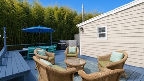 Una terrazza con mobili in vimini, un barbecue e un ombrello blu.