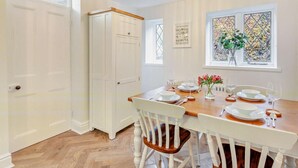 A dining area with a wooden table set for four, white chairs, a chandelier, a window with a view, and a white door. - 2 Bed in Alnwick (oc-93093) (Lemmington Hall)