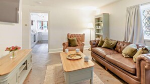A living room with a brown leather sofa, a wooden coffee table, a white armchair, and a bookshelf. - 2 Bed in Alnwick (oc-93093) (Lemmington Hall)
