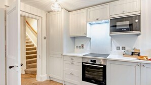 A modern kitchen with white cabinetry, a Bosch oven, a microwave, and a staircase leading to another room. - 2 Bed in Alnwick (oc-93093) (Lemmington Hall)